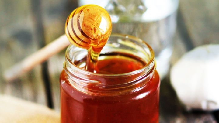 Ein Glas Honig steht neben einem kleinen Glas Wasser, w&auml;hrend ein L&ouml;ffel Honig aus dem Glas tropft &ndash; ideal f&uuml;r Honigwasser.