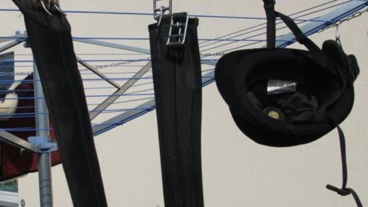 Drei schwarze Hosen h&auml;ngen auf einer W&auml;schespinne zum Trocknen in einem Au&szlig;enbereich mit heller Wand.