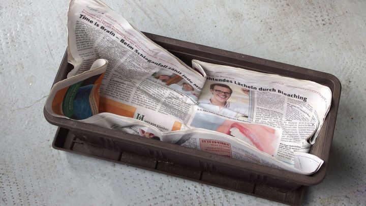 Ein Balkonkasten liegt auf einem Tisch, ausgelegt mit zerkn&uuml;llten Zeitungen, die als Schicht zum Bef&uuml;llen dienen.