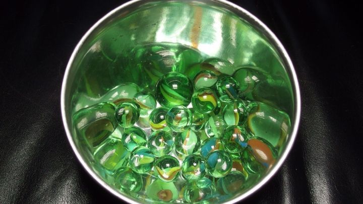 Eine silberne Sch&uuml;ssel enth&auml;lt viele Glasmurmeln, die bunten und gr&uuml;nen Farben reflektieren, in einem beruhigenden Ambiente.