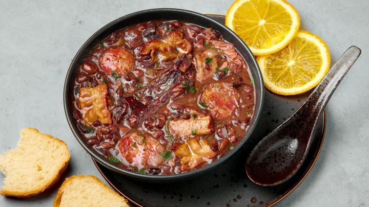 Ein herzhafter Bohneneintopf mit Kassler liegt in einer Sch&uuml;ssel, umgeben von frischem Brot und Zitronenscheiben.
