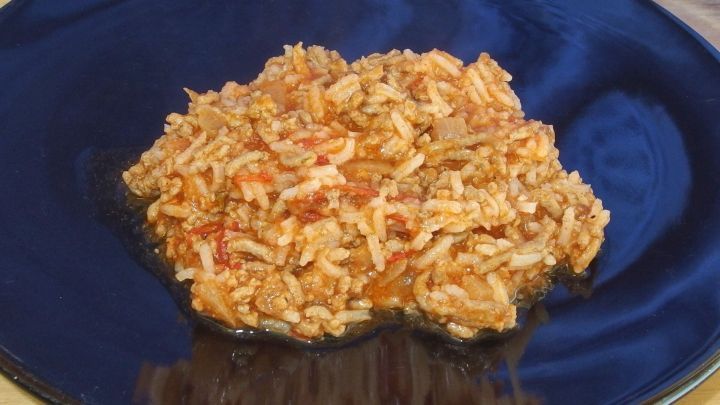 Auf einem blauen Teller liegt eine portionierte Reispfanne mit Gem&uuml;se und Hackfleisch, appetitlich angerichtet und dampfend.