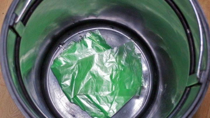 Ein M&uuml;llbeh&auml;lter zeigt eine gr&uuml;ne M&uuml;llt&uuml;te, die am Boden liegt. Die T&uuml;te ist sichtbar, der Eimer ist leer.