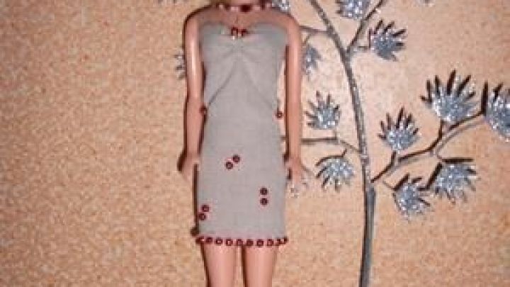 Eine Barbie-Puppe tr&auml;gt ein elegantes Kleid aus elastischer Binde, umgeben von modernem Kunstwerk im Hintergrund.