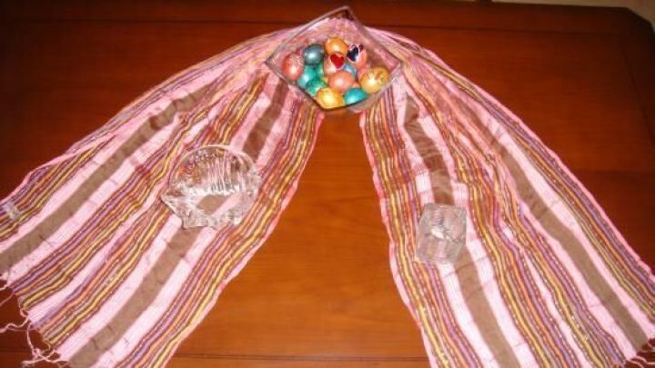 Bunte Schals liegen dekorativ &uuml;ber einem Tisch und umrahmen eine Sch&uuml;ssel mit bunten, gef&auml;rbten Eiern.