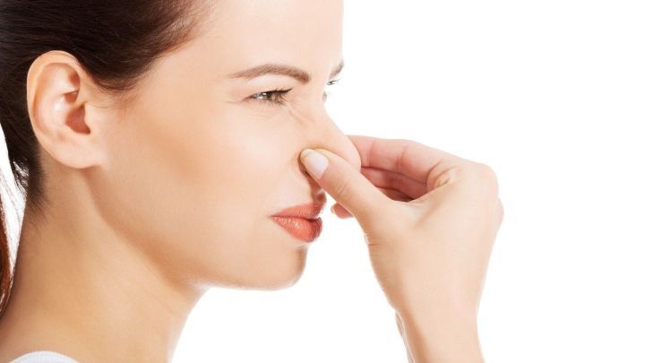 Eine Frau h&auml;lt sich die Nase zu, um einen unangenehmen Geruch zu vermeiden, w&auml;hrend sie in einem hellen Raum steht.