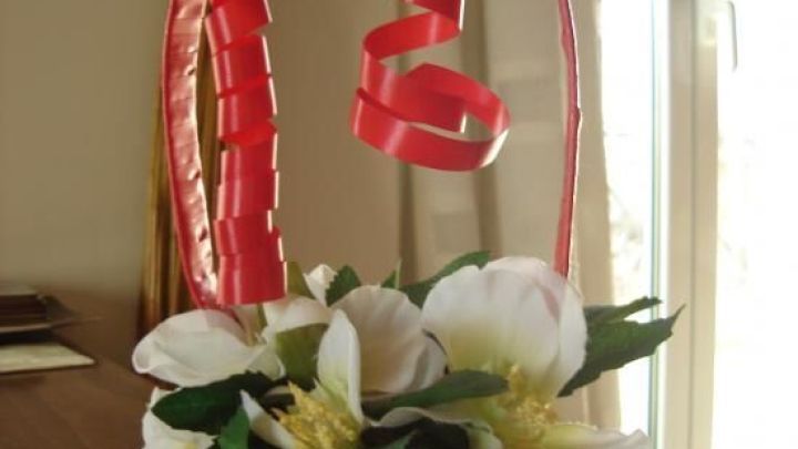 Ein rot dekorierter Korb mit Seife und Blumen steht auf einem Tisch, von einem hellen Raum mit Fenstern umgeben.