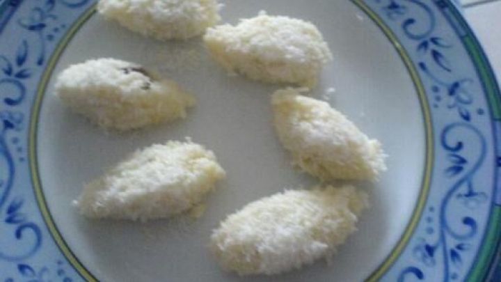 Auf einem Teller liegen selbstgemachte Raffaello, die mit Kokosraspeln &uuml;berzogen sind, in einer hellen K&uuml;che.