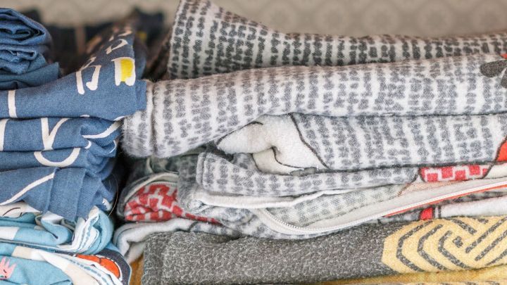 Faltbare Kleider liegen ordentlich aufeinander gestapelt, w&auml;hrend der Hintergrund eine gemusterte Wand zeigt.