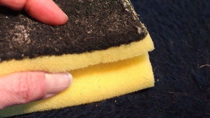 Ein Topfschwamm wird in der Hand gehalten, w&auml;hrend er &uuml;ber einen Kratzbaum mit Katzenhaaren gestrichen wird.