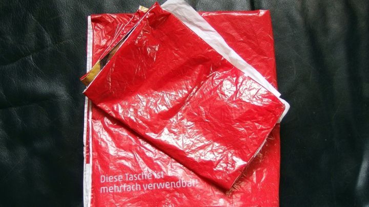 Rote Plastikt&uuml;ten liegen &uuml;ber einem Paket und zeigen, dass sie als Versandtaschen verwendet werden, um Inhalte zu sch&uuml;tzen.