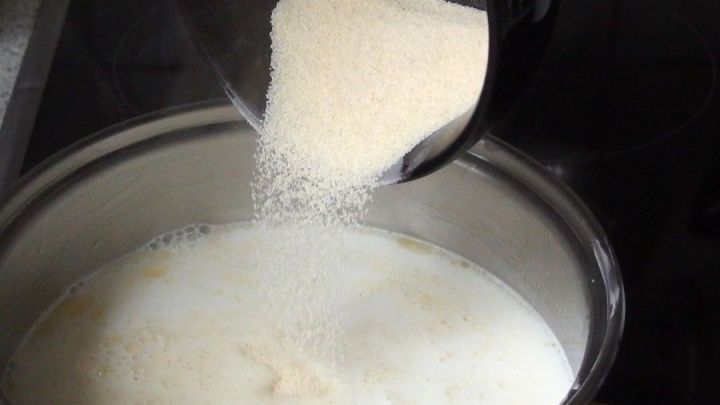 Grie&szlig; wird in einen Topf mit Milch gegossen, um unges&uuml;&szlig;ten Grie&szlig;brei zu kochen. Eine einfache K&uuml;chensituation.