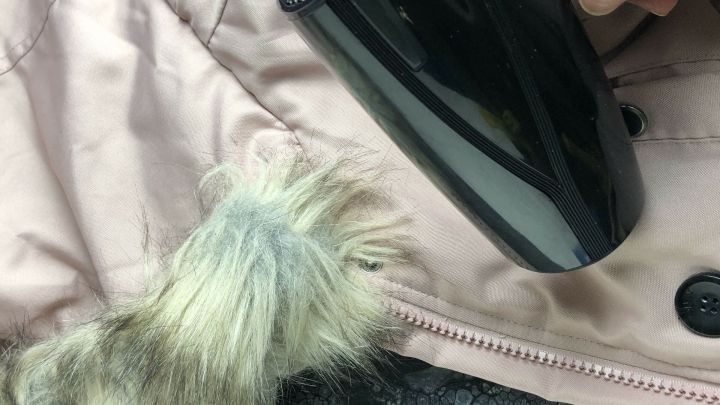 Ein schwarzer Haarf&ouml;n wird auf einen Winterjacken&auml;rmel mit Pelzbesatz gerichtet, um Kerzenwachs zu entfernen.