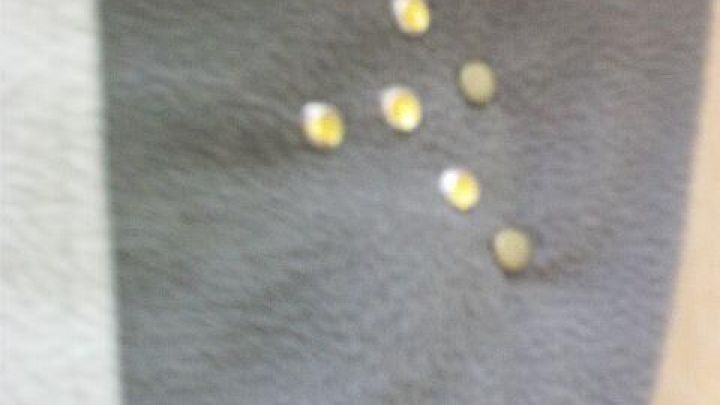 Ein graues Kleidungsst&uuml;ck hat einen kleinen Riss, der mit gl&auml;nzenden, gelben Steinen verziert ist.