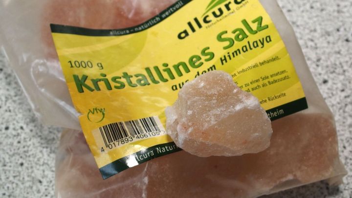 Ein Beutel mit Kristallsalz liegt auf einer K&uuml;chenoberfl&auml;che, w&auml;hrend sich ein gro&szlig;es St&uuml;ck Salz daneben befindet.