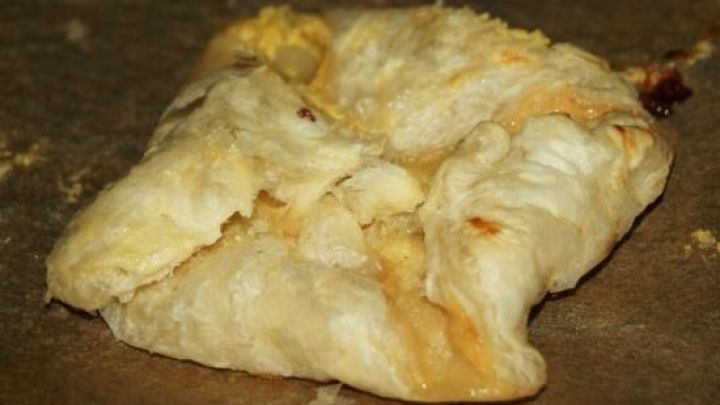 Ein gebackenes Bl&auml;tterteigt&auml;schchen mit Vanille und Apfel liegt auf einem Blech, leicht ausgebacken und goldbraun.