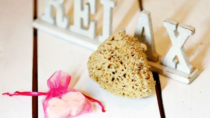 Eine Badekugel liegt neben einem Dekorationswort &bdquo;RELAX&ldquo; auf einer hellen Holzoberfl&auml;che, was Entspannung signalisiert.