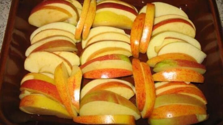 In einer braunen Auflaufform liegen gleichm&auml;&szlig;ig geschnittene Apfelscheiben bereit f&uuml;r ein k&ouml;stliches Apple-Crumble.