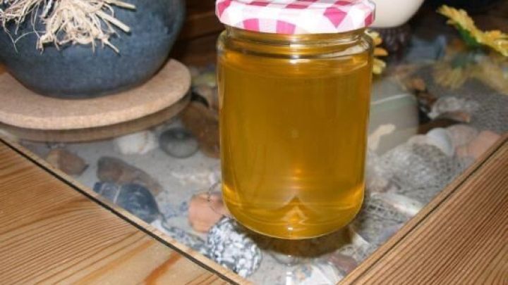 Ein Glas L&ouml;wenzahnbl&uuml;tengelee steht auf einem Tisch, umgeben von dekorativen Steinen und Blumen.