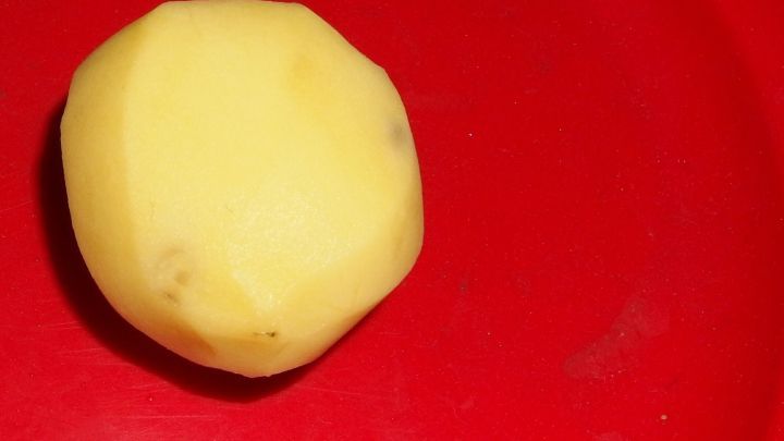 Eine rohe Kartoffel liegt auf einem roten Teller, bereit, gegen Brandwunden eingesetzt zu werden.