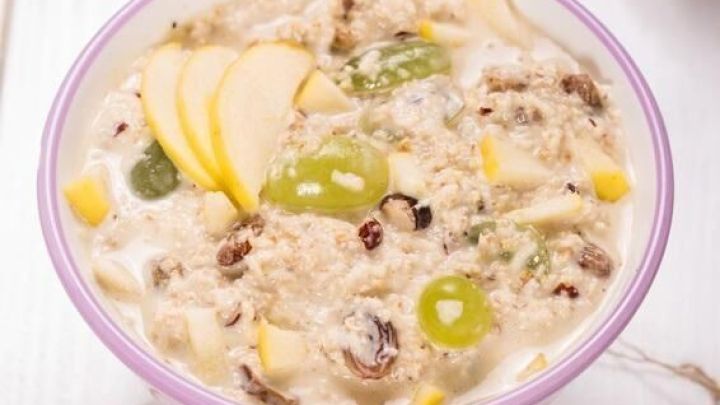 Eine Sch&uuml;ssel Original Schweizer Bircher M&uuml;sli mit Haferflocken, Trauben, Apfelst&uuml;cken und N&uuml;ssen auf einem wei&szlig;en Tisch.