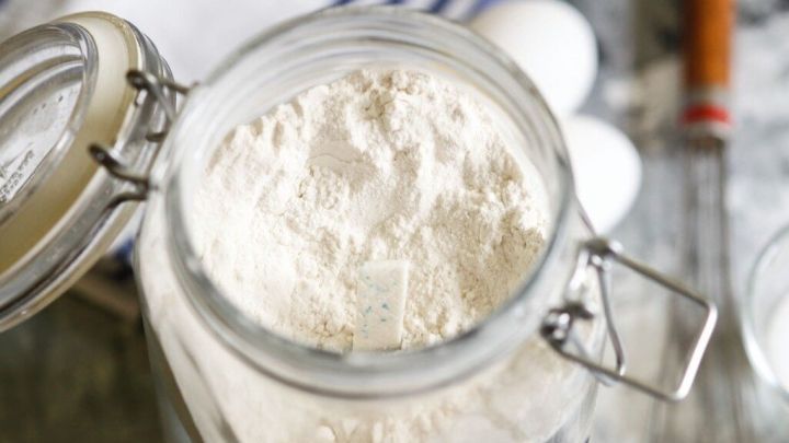 Ein Glas mit Mehl steht auf einer Arbeitsfl&auml;che, umgeben von Eiern und einem Schneebesen, bereit zum Backen.