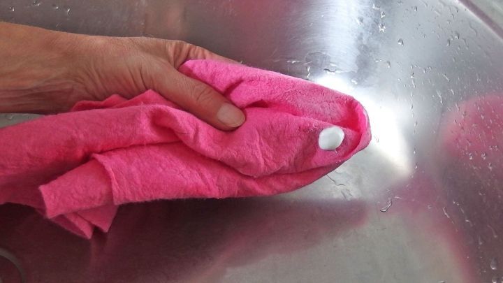 Ein Handtuch in Rosa reinigt ein Edelstahl Waschbecken, um es gl&auml;nzend und sauber zu halten.