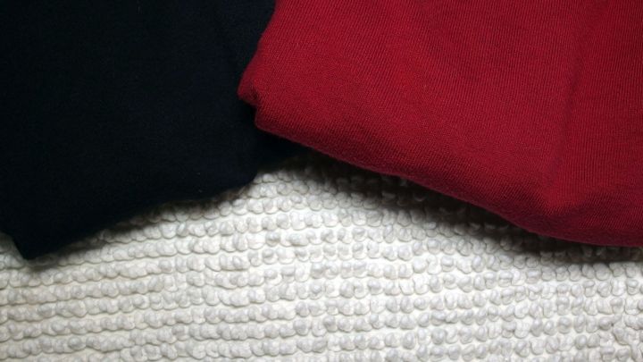 Schwarz und rot gefaltete Kleidung liegt auf einem Teppich, ideal zum W&auml;sche vorsortieren in mehreren W&auml;schek&ouml;rben.