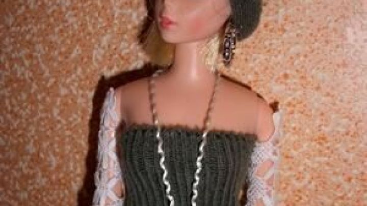 Eine Barbie-Puppe tr&auml;gt ein Outfit aus einem Socken und Spitze, mit einem modischen Accessoire vor einer gemusterten Wand.