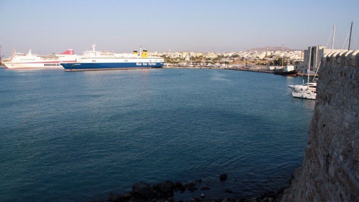 Ein ruhiges Hafenbecken zeigt verschiedene Schiffe, w&auml;hrend die Sonne am Horizont &uuml;ber der Stadt scheint.