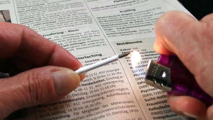 Ein Kugelschreiber wird mit einem Feuerzeug angez&uuml;ndet, w&auml;hrend er auf einer Zeitungsseite liegt.