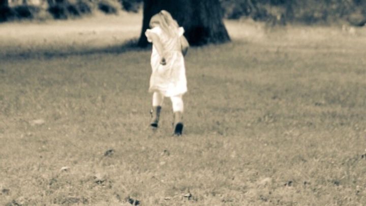 Ein kleines Kind in einem wei&szlig;en Kleid l&auml;uft fr&ouml;hlich &uuml;ber eine gr&uuml;ne Wiese, umgeben von B&auml;umen und Natur.