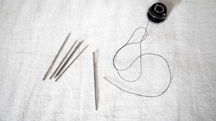 Nadeln und Faden liegen auf wei&szlig;em Stoff, bereit zum N&auml;hen, in einer ordentlichen und &uuml;bersichtlichen Anordnung.