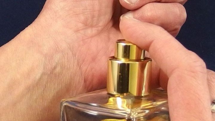 Eine Hand h&auml;lt eine Parf&uuml;mflasche, w&auml;hrend der Spr&uuml;hkopf gedr&uuml;ckt wird, um den Duft freizusetzen und die Haut einzu&ouml;len.