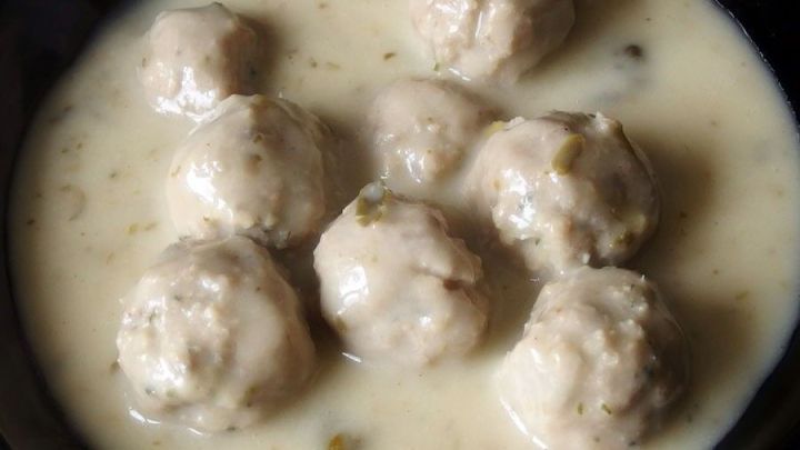 Klopse liegen in einer hellen Kr&auml;utersauce, umgeben von einem dunklen Geschirr, bereit zum Servieren.