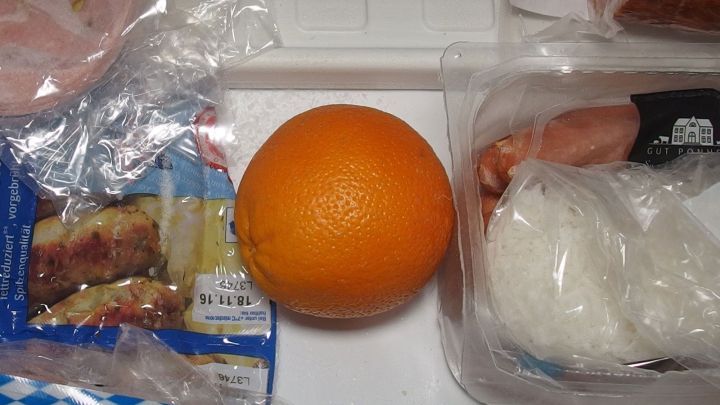 Eine Orange liegt auf einer Arbeitsfl&auml;che, umgeben von Verpackungen, bereit zum Schneiden f&uuml;r feine Orangenmarmelade.