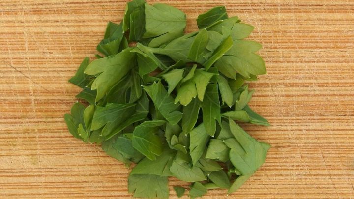 Gehackte Petersilie liegt auf einem Holzbrett und wartet darauf, Gerichte mit Knoblauch zu verfeinern.