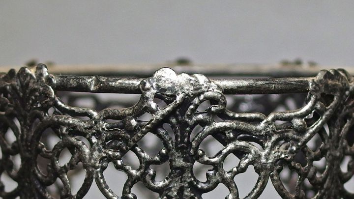 Ein filigraner Zinnring wird gereinigt, w&auml;hrend er auf einem neutralen Hintergrund steht, was die Detailarbeit hervorhebt.