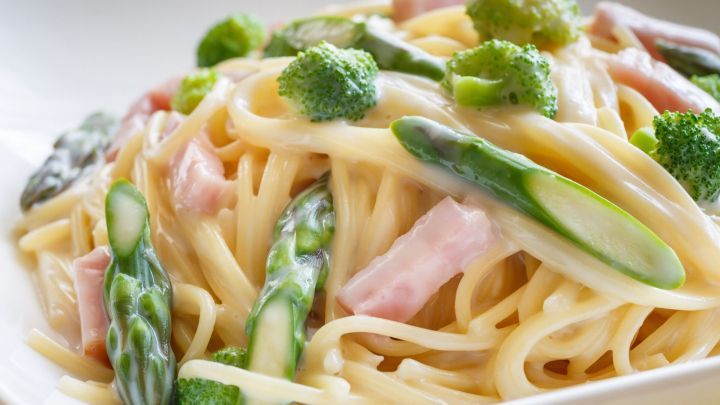 Gr&uuml;ner Spargel und Broccoli liegen &uuml;ber cremigen Spaghetti mit etwas Schinken in einer wei&szlig;en Sch&uuml;ssel.
