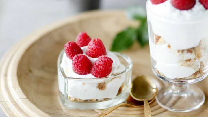 Zwei Desserts mit Himbeeren liegen auf einem Holzbrett, frisch mit Sahne und knusprigen Schichten, umgeben von Beeren.