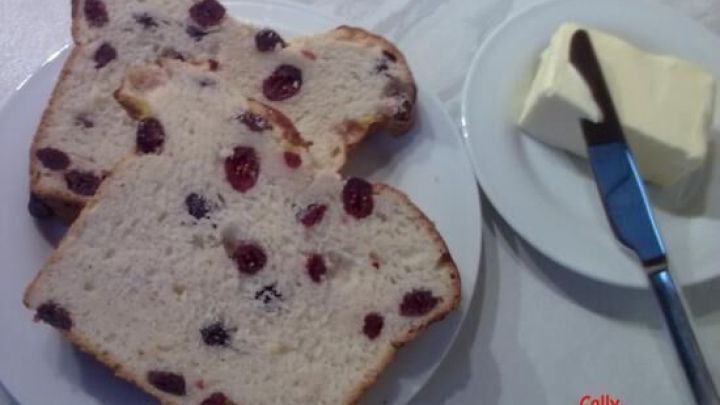 Scheiben von Cranberry-Brot liegen auf einem Teller, w&auml;hrend ein St&uuml;ck Butter mit einem Messer daneben serviert wird.