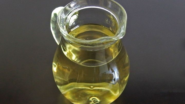 Ein transparentes Glasgef&auml;&szlig; mit goldenem &Ouml;l steht auf einem dunklen Tisch, bereit zur Verwendung bei Dammriss-Beschwerden.