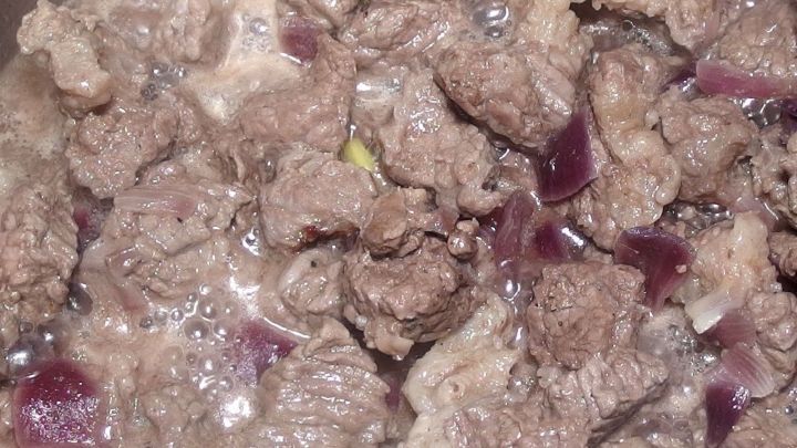 Gulasch aus zartem Rindfleisch kocht in einer Pfanne, umgeben von feinen Zwiebelst&uuml;cken f&uuml;r den authentischen Geschmack.