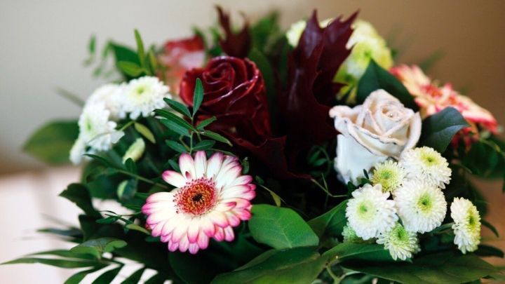 Ein bunter Blumenstrau&szlig; mit verschiedenen Blumen und Bl&auml;ttern steht in einer Vase auf einem Tisch, strahlt Sch&ouml;nheit aus.