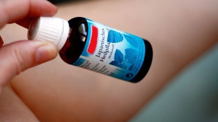 Ein Hand h&auml;lt eine Flasche japanisches Heilpflanzen&ouml;l, w&auml;hrend es auf den schmerzendem Kniegelenk aufgetragen wird.