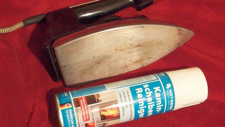 Ein B&uuml;geleisen liegt neben einer Spraydose f&uuml;r Kamin- und Ofenreiniger auf einem roten Untergrund.