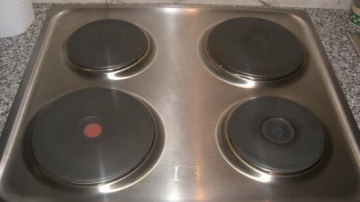 Ein Edelstahl Kochfeld mit vier Kochplatten, sauber und unbenutzt, auf einer grauen, strukturierten K&uuml;chenarbeitsplatte.