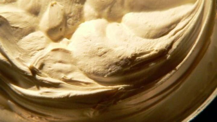 Die Creme zeigt eine dichte, cremige Textur in einer offenen Dose, bereit zur Anwendung in einem dunklen Umfeld.