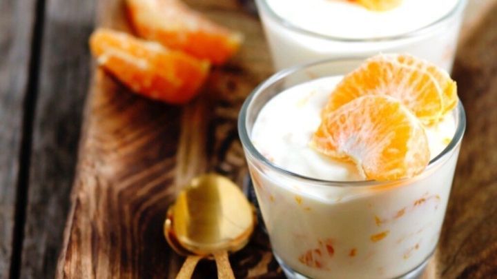 Quarkpudding mit Mandarinen in Gl&auml;sern auf einem Holzbrett, garniert mit Mandarinenst&uuml;cken, in einer gem&uuml;tlichen K&uuml;chenszene.