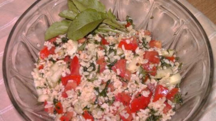 Ein Bulgursalat mit Tomaten, Gurken und Kr&auml;utern in einer Glassch&uuml;ssel, garniert mit frischen Salatbl&auml;ttern auf einem Tuch.